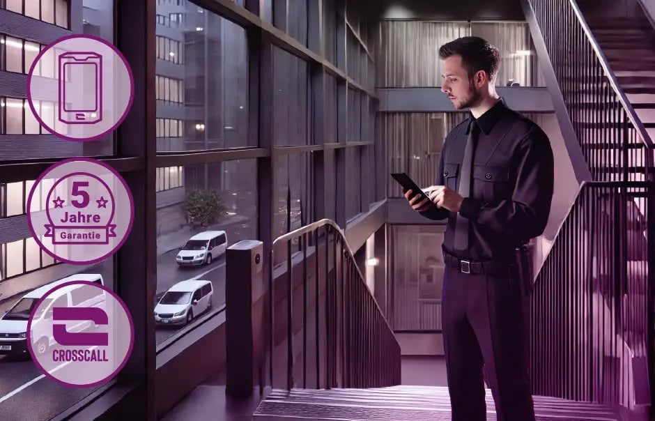 Un agent de sécurité se tient seul dans une cage d'escalier la nuit, un smartphone CROSSCALL à la main.