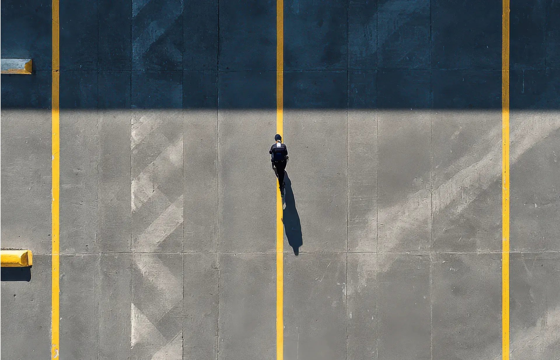 Top view of a security guard on patrol through a car park, geometric patterns of parking lines and pillars, a lone figure conveying a sense of surveillance and control