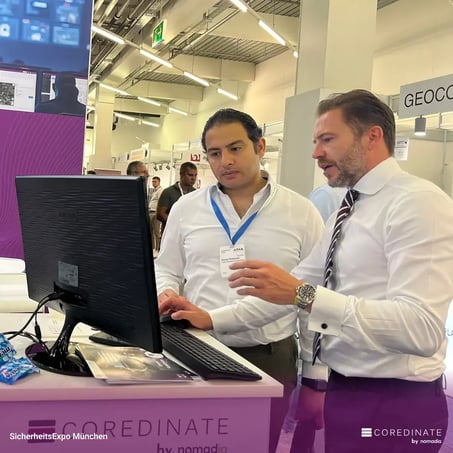 Sebastian Kulig erklärt einem Messebesucher etwas am Computerbildschirm am COREDINATE®-Stand auf der SicherheitsExpo München.