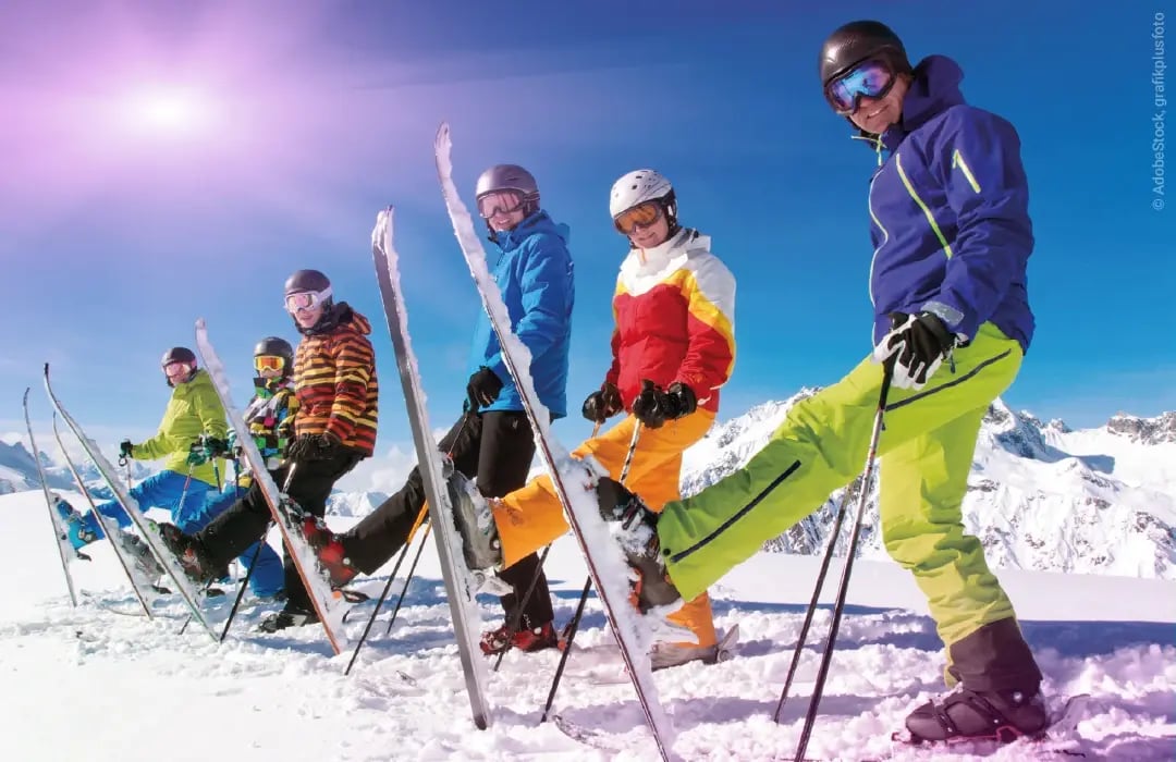 Eine Gruppe Skifahrer steht mit Skiern im Schnee bei blauem Himmel und Sonnenschein