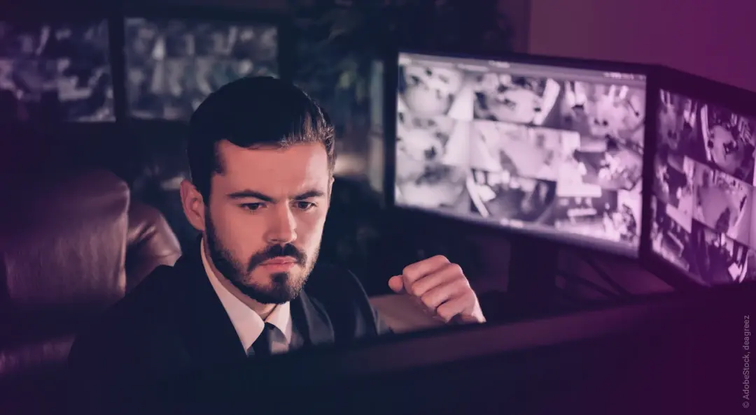 Sicherheitsmitarbeiter vor Bildschirmen in Überwachungszentrale